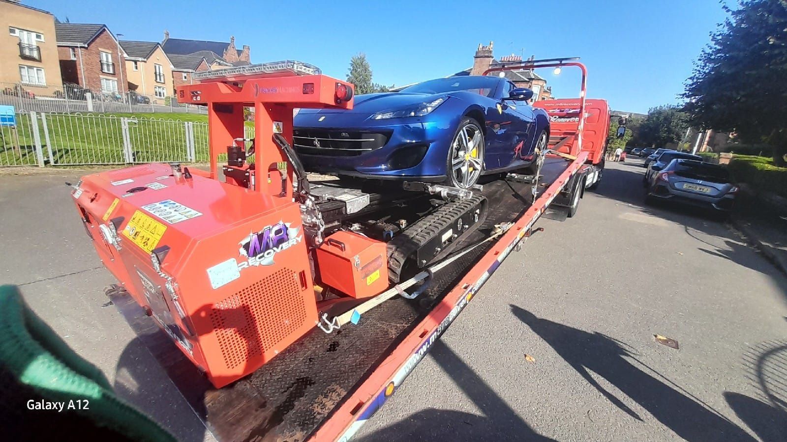 Blue sports car on a flatbed tow truck. Sunny day in a residential area.