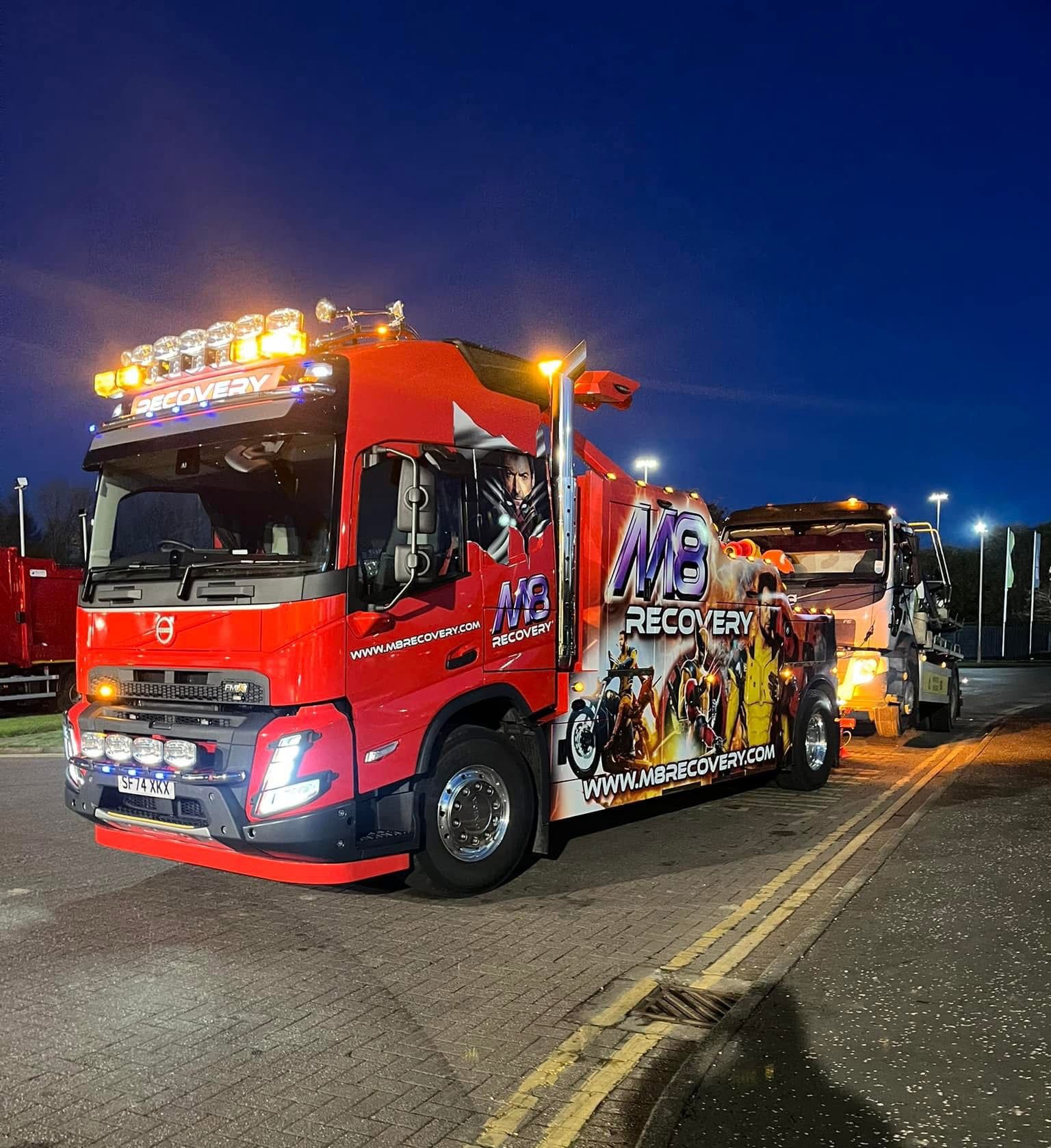 Red tow truck hauling another truck at night.