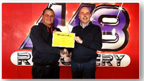 Two men holding a certificate with a logo in the background.