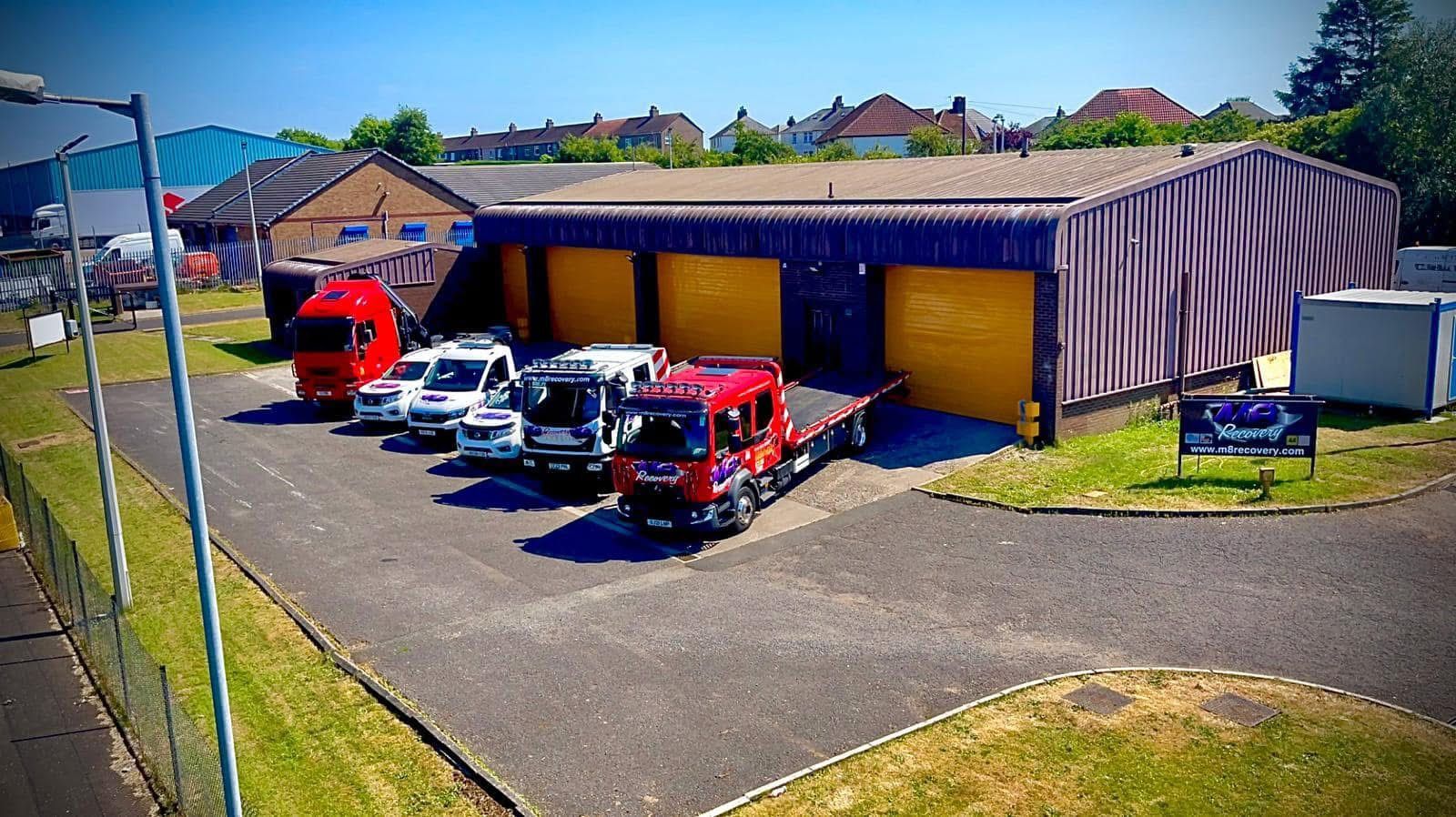 Vehicles parked outside a garage with yellow doors, under a bright blue sky.