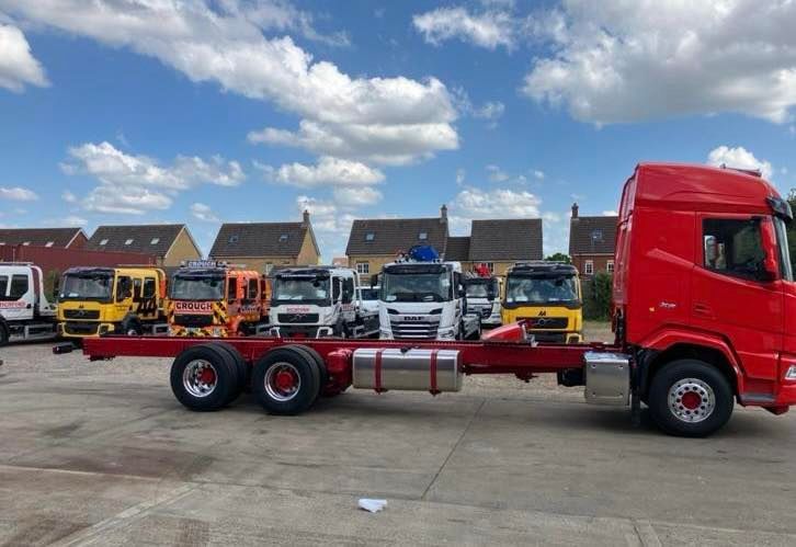 Red cab and chassis truck parked, other trucks in background under a cloudy sky.