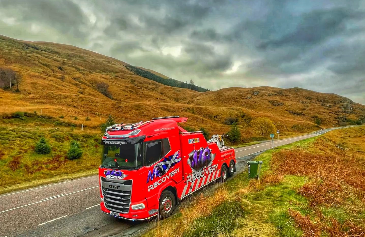 Red tow truck on road in mountainous, autumn landscape.