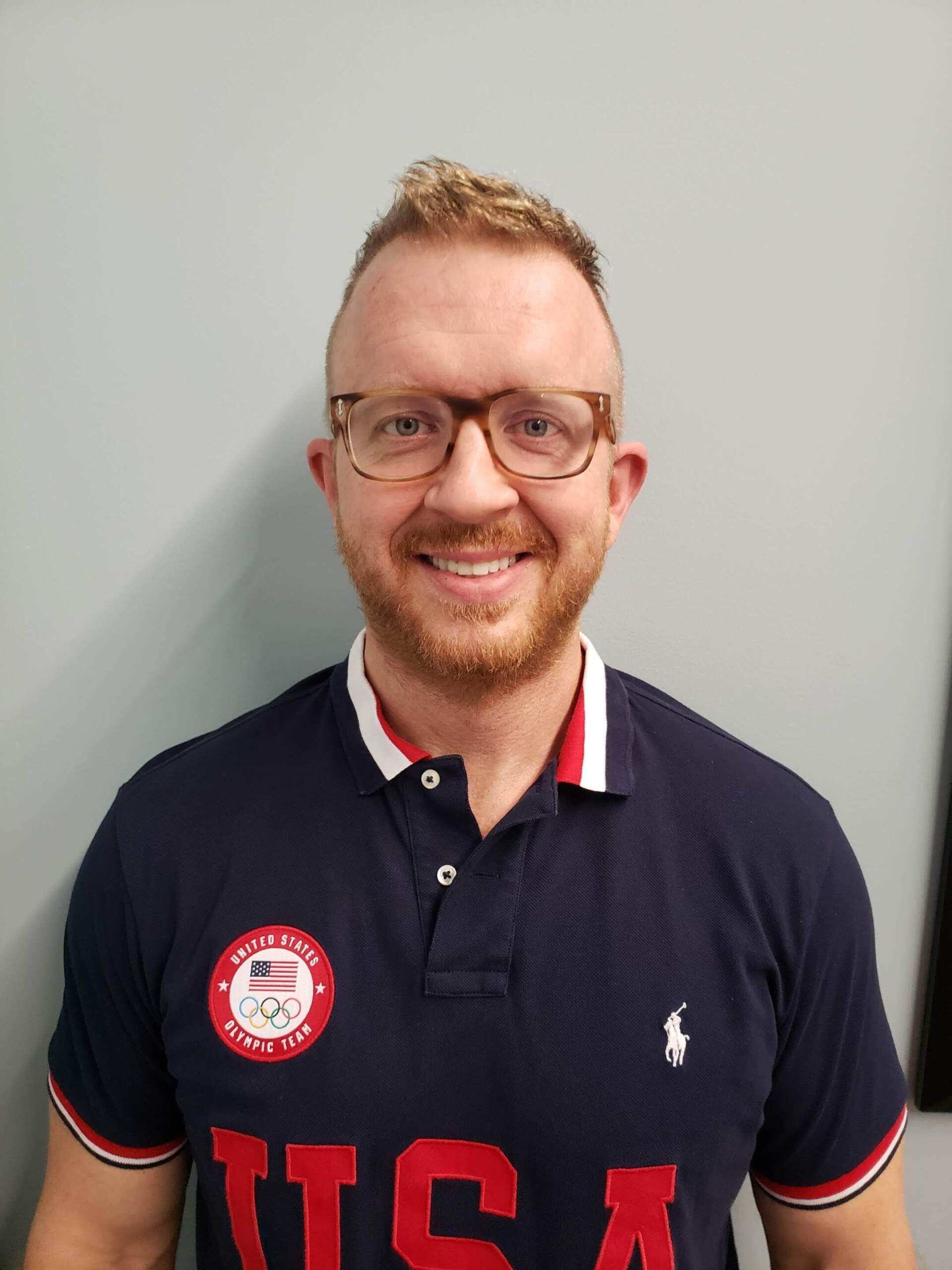 A man wearing glasses and a usa polo shirt is smiling for the camera.