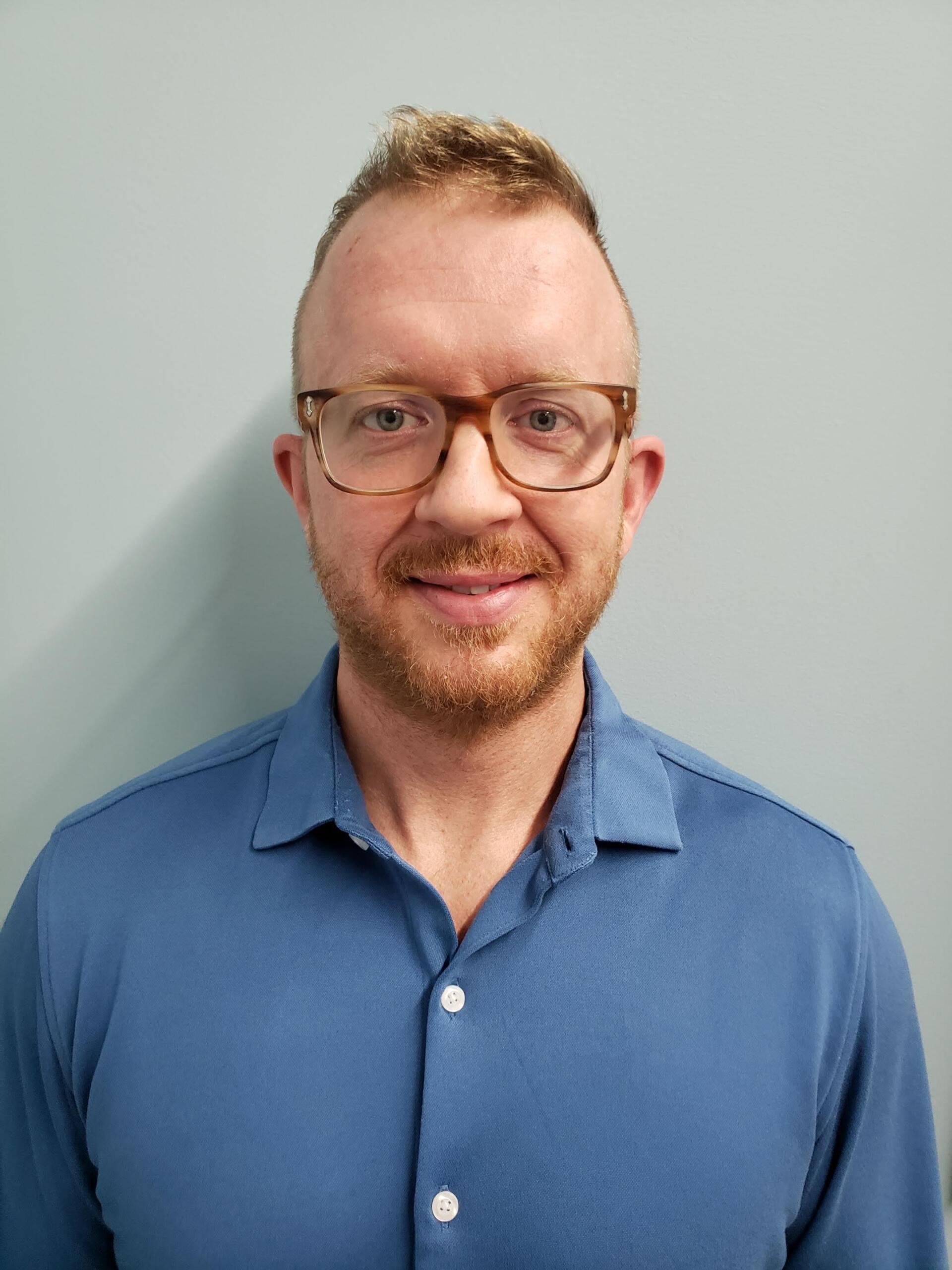 A man wearing glasses and a blue shirt is smiling for the camera.