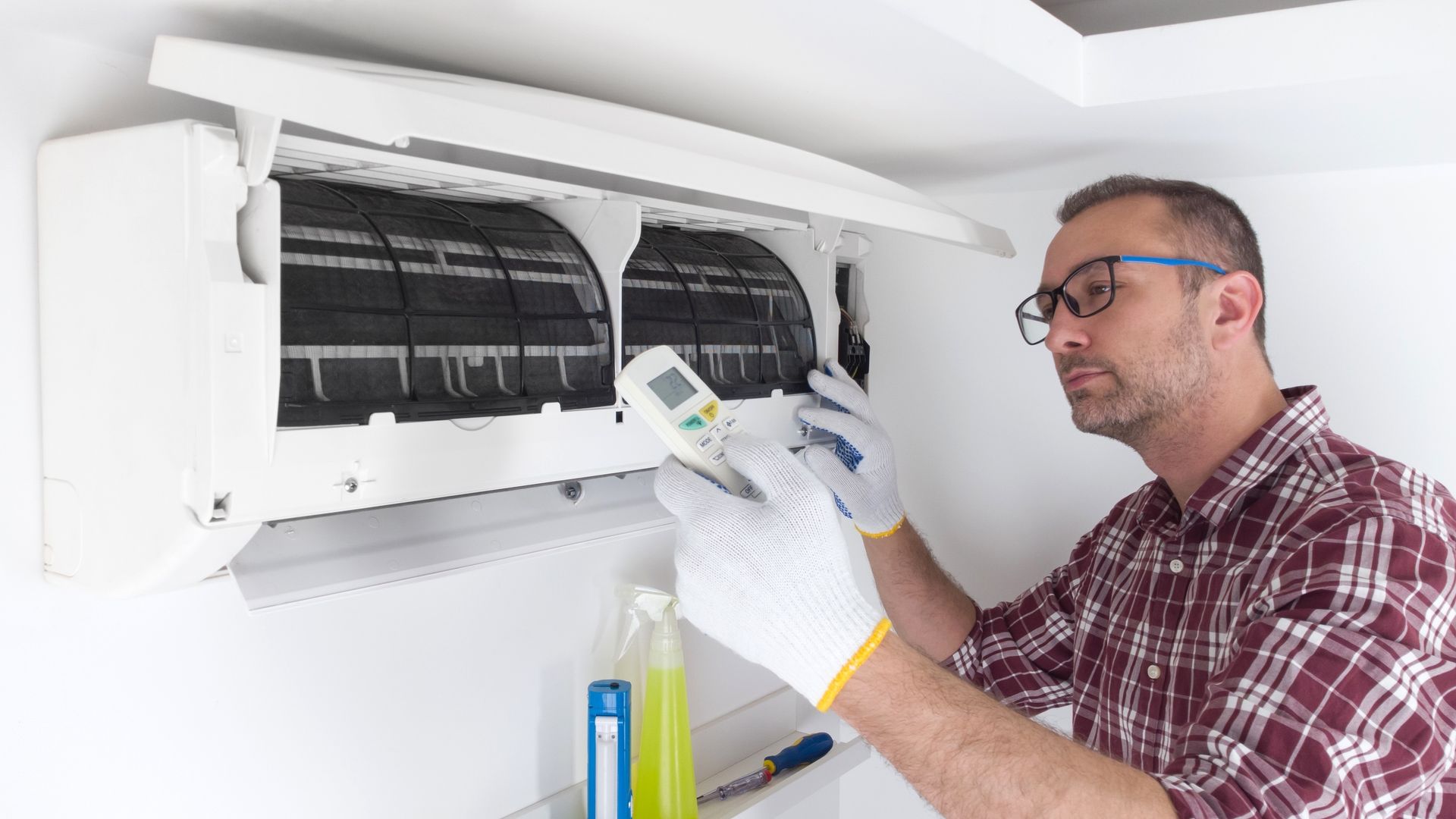 Technician cleaning a wall-mounted air conditioner with a spray bottle and cloth