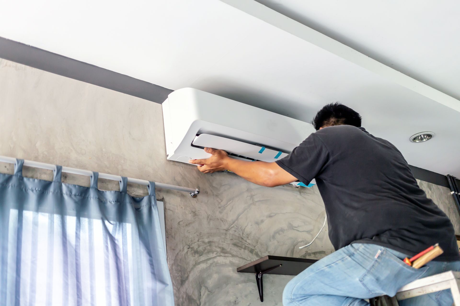 Technician repairing a wall-mounted air conditioner indoors beneath a ceiling beam