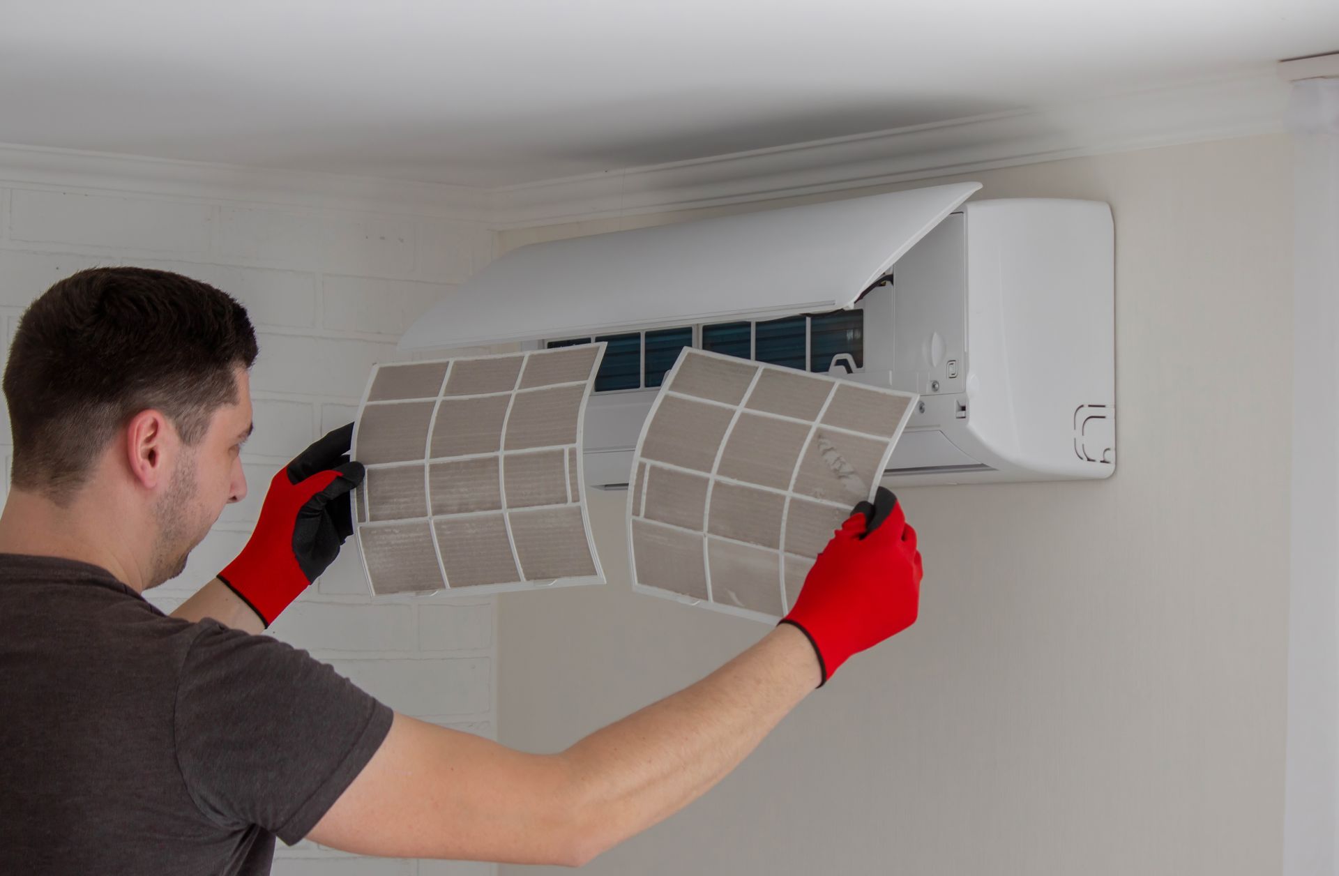 Person installing or cleaning a wall-mounted air conditioner filter with red gloves