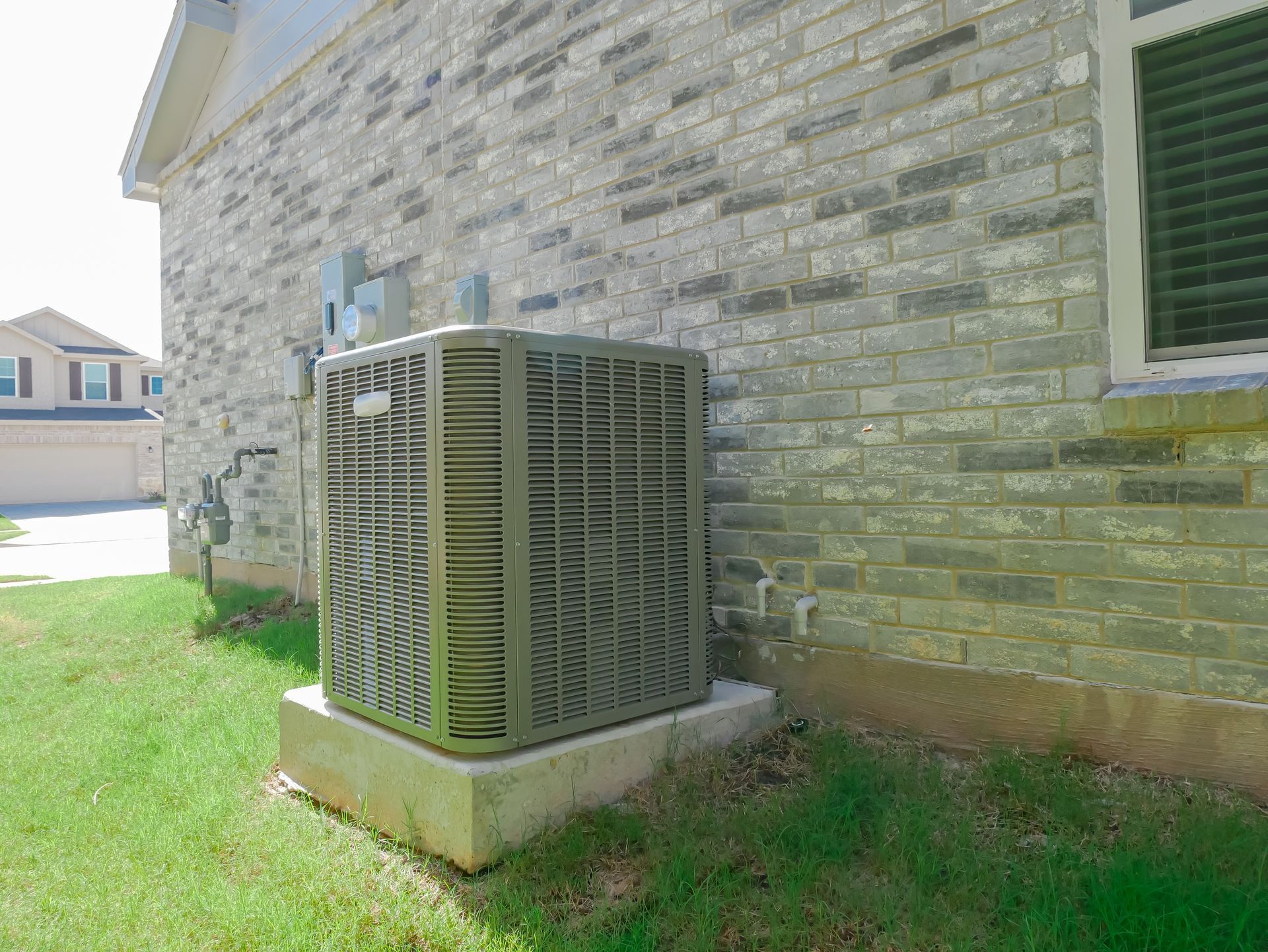 Outdoor air conditioner unit beside a stone house wall on a grassy lawn