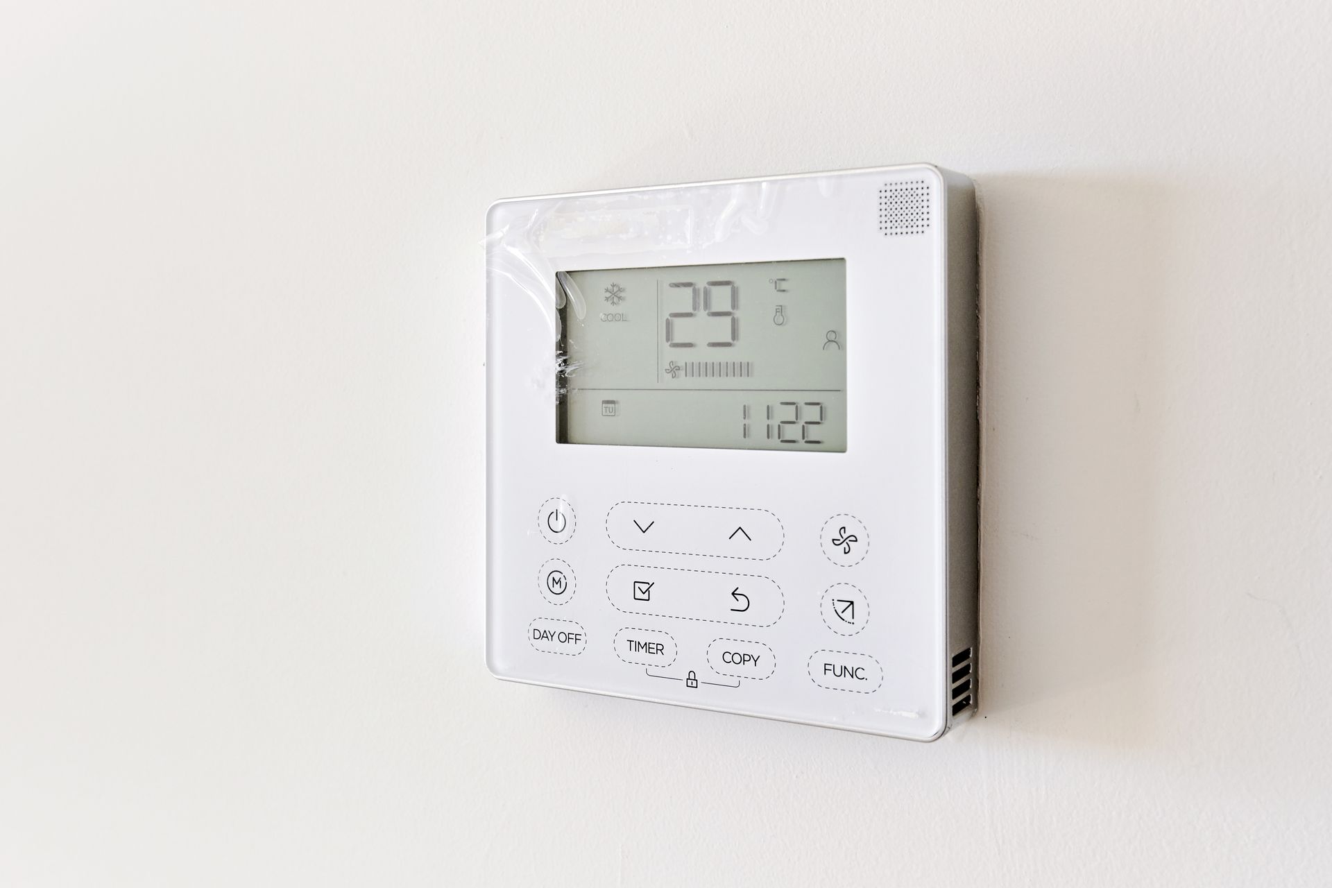 White wall-mounted digital thermostat displaying 29°C in a minimalist room.