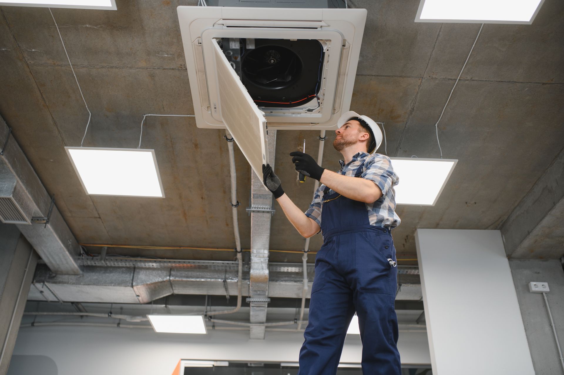 Technician adjusting a ceiling-mounted HVAC vent in a commercial interior