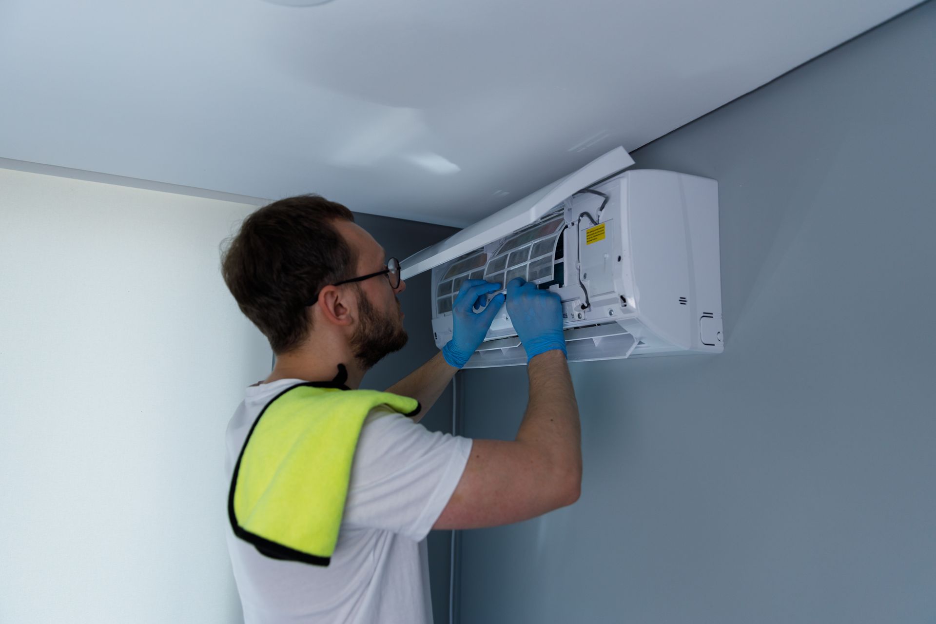 Technician installing an air conditioner indoors with a drill, wearing gloves and a high-visibility vest