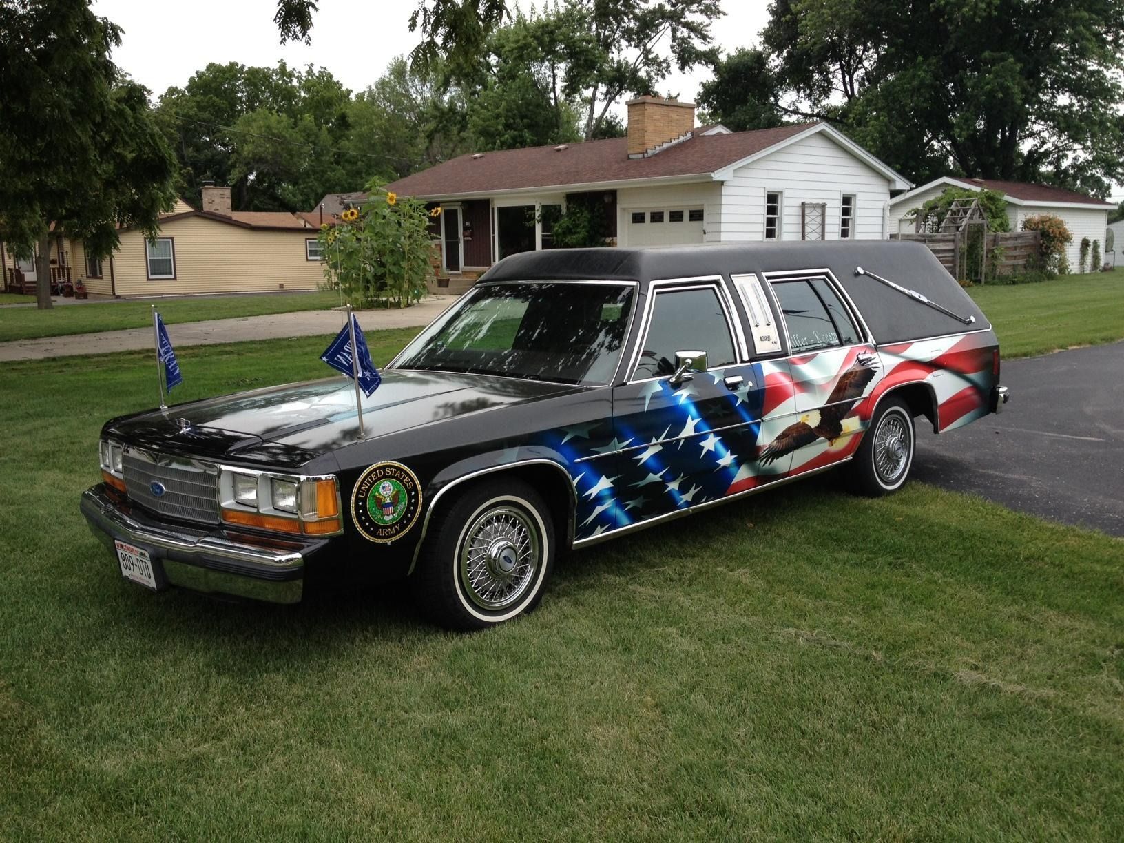 Custom black hearse with American flag graphics parked on a lawn in front of a house.