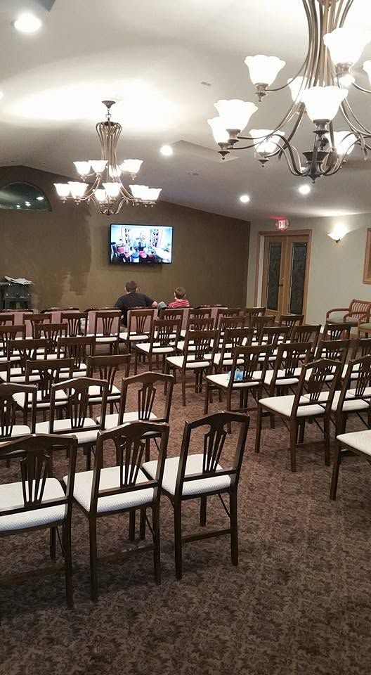 Empty conference room with rows of chairs, chandeliers, and a wall-mounted TV near the front