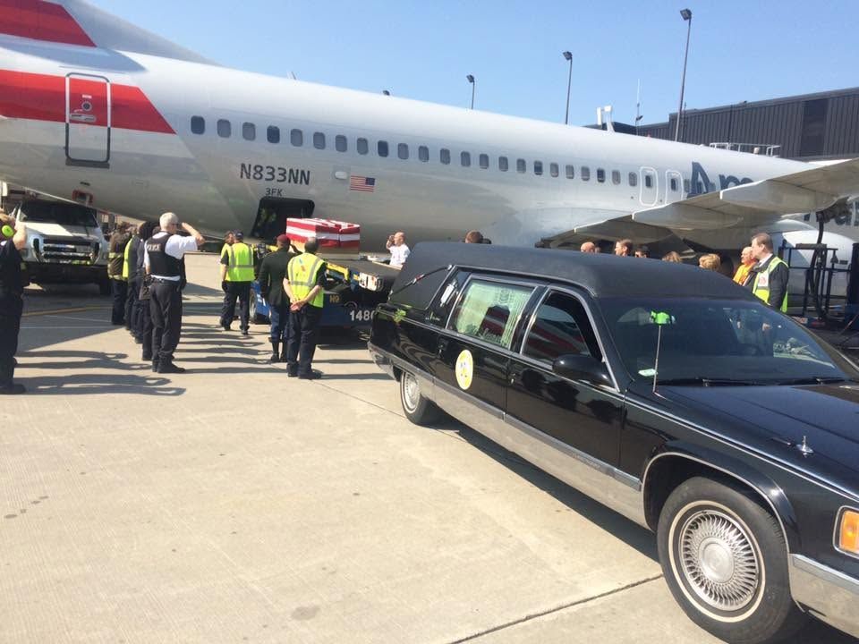 Black hearse on tarmac near a British Airways plane with uniformed people nearby