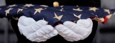 White-gloved hands holding a folded American flag with white stars on a blue field
