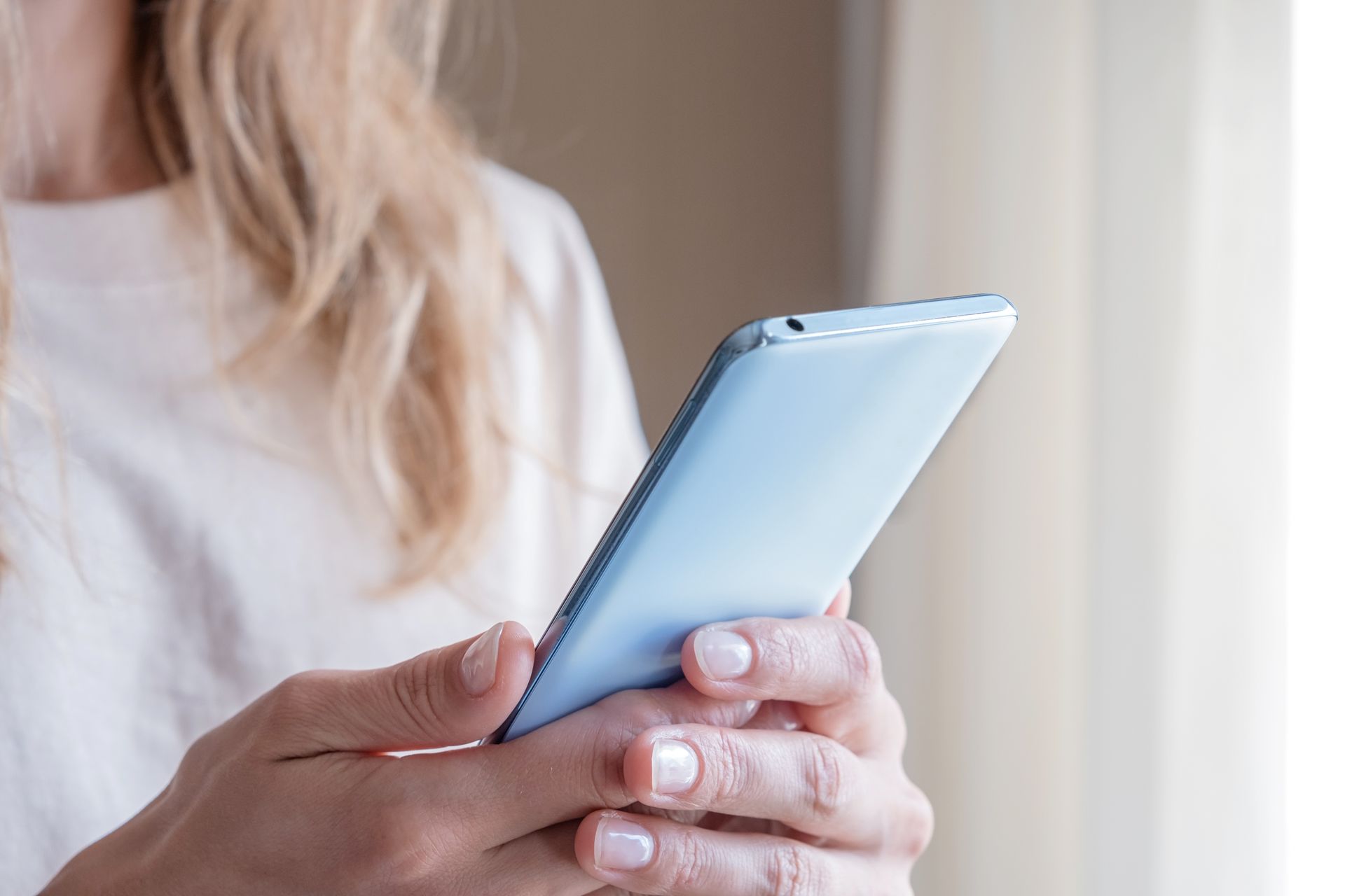 Hands holding a light blue smartphone in a bright indoor setting