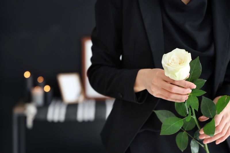 Person in a black suit holding a white rose at a softly lit indoor event table.