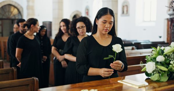 People in black attire stand in a church aisle holding white roses during a solemn ceremony