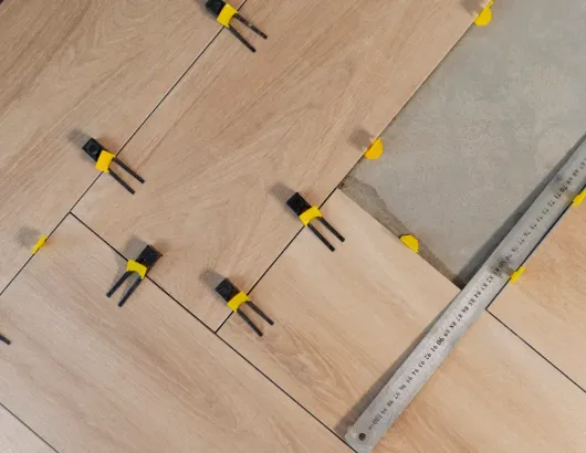 Tile installation with wedges and a metal ruler measuring diagonal cuts on wood-look flooring.