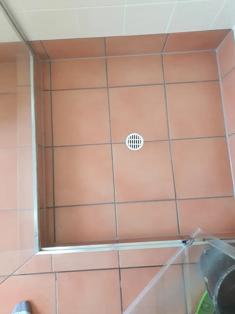 Tiled shower floor with a central drain and a glass shower door edge visible.