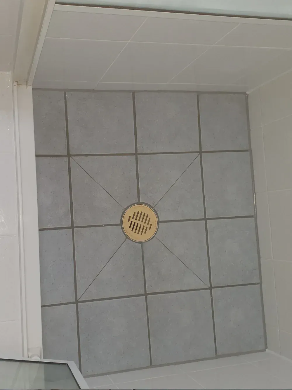 Tiled shower floor with a round yellow drain cover in the center