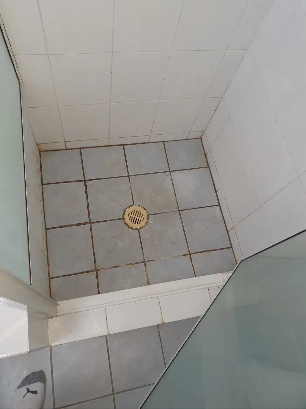 Small tiled shower stall with a center drain and glass door on the right.
