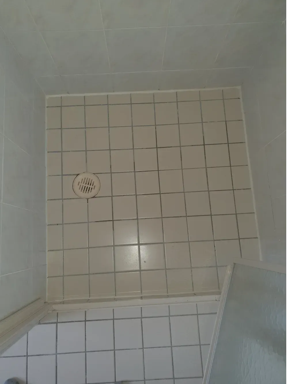 Tiled shower floor with a round drain and a shower seat in the corner.