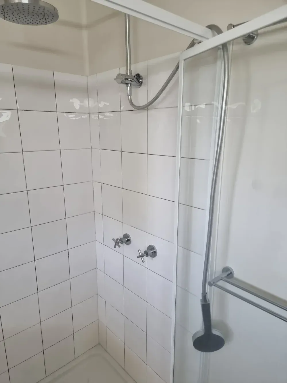 Small tiled shower stall with handheld showerhead and metal grab bar