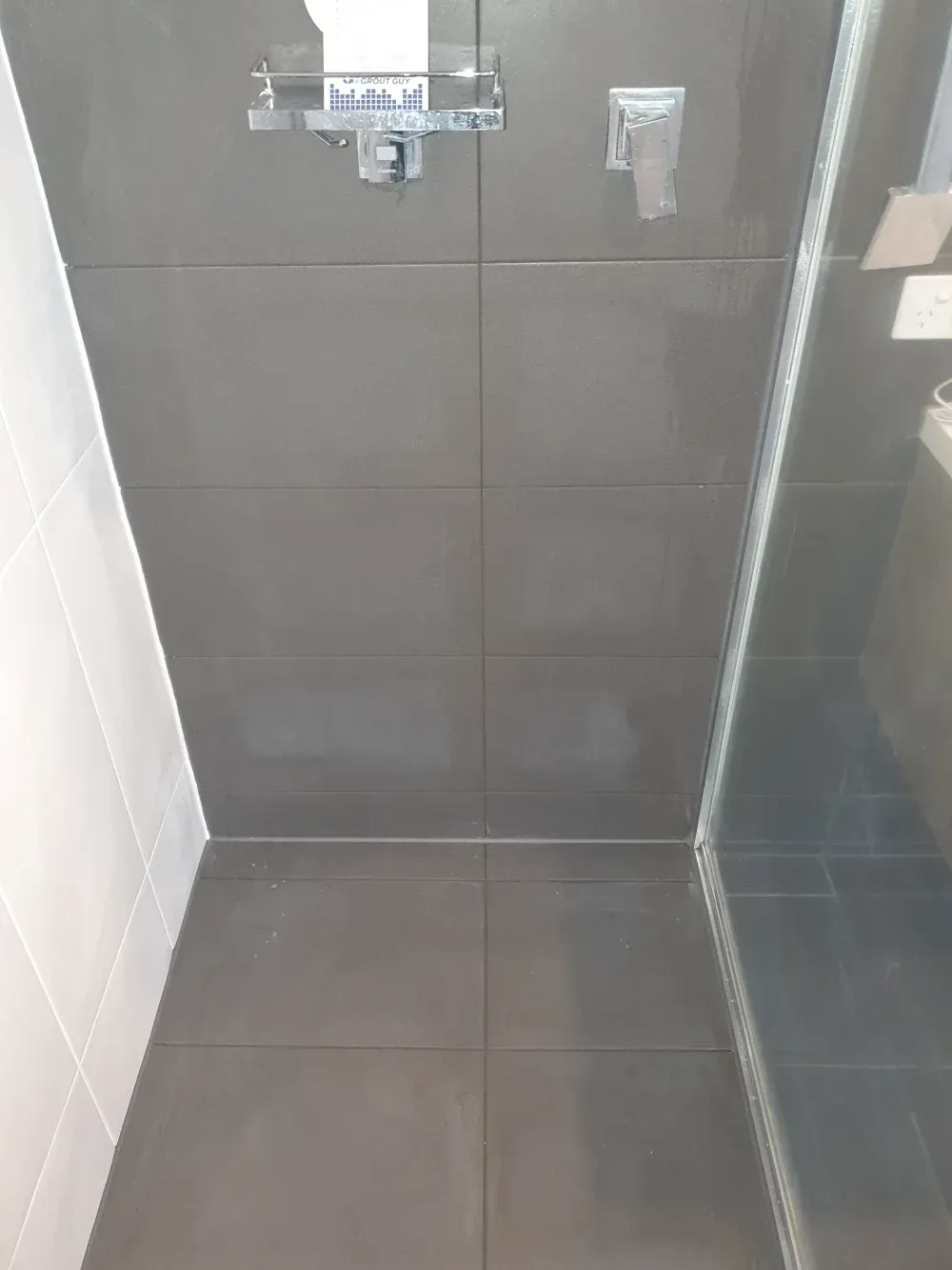 Small tiled shower stall with dark gray walls, floor drain, and glass door.