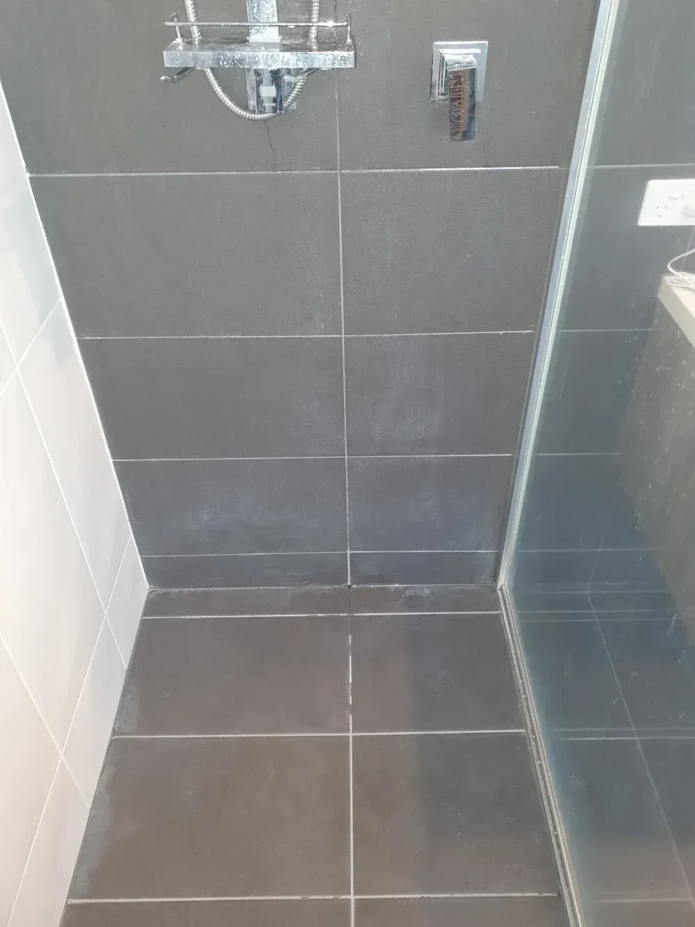 Small tiled shower stall with dark gray walls, floor drain, and chrome fixtures