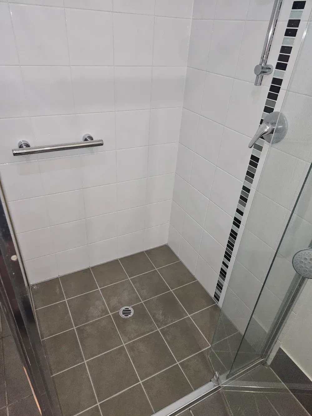 Accessible shower with tiled floor, grab bar, and glass door in a small bathroom.