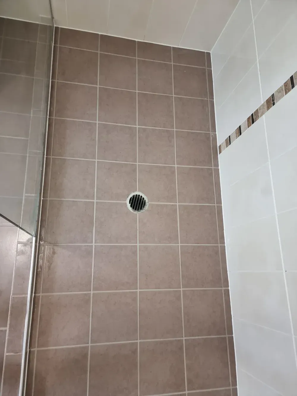 Tiled bathroom wall with a circular drain and white shower tiles on the right