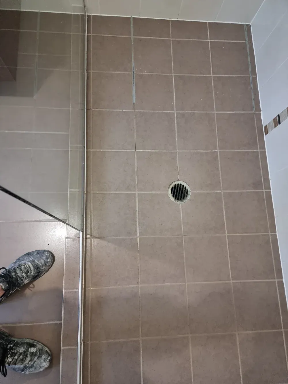 Tiled bathroom floor with a floor drain and two muddy shoes at the bottom left