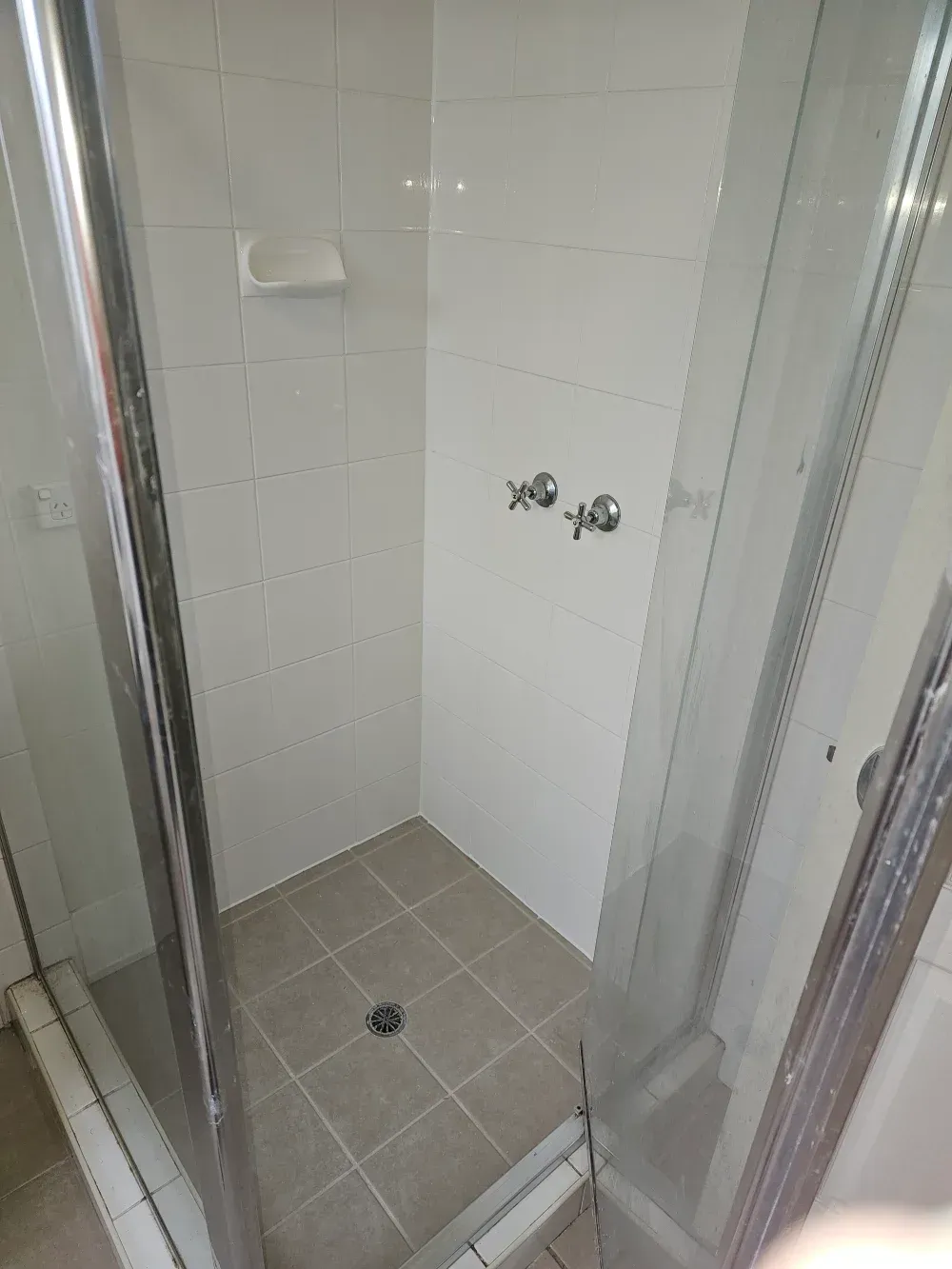 Small tiled shower stall with glass doors, white walls, and a drain in the floor.