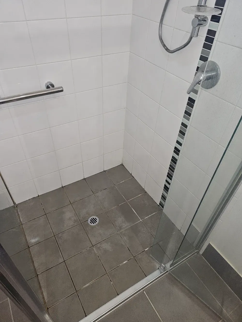 Empty tiled shower with a floor drain, grab bar, and glass door.