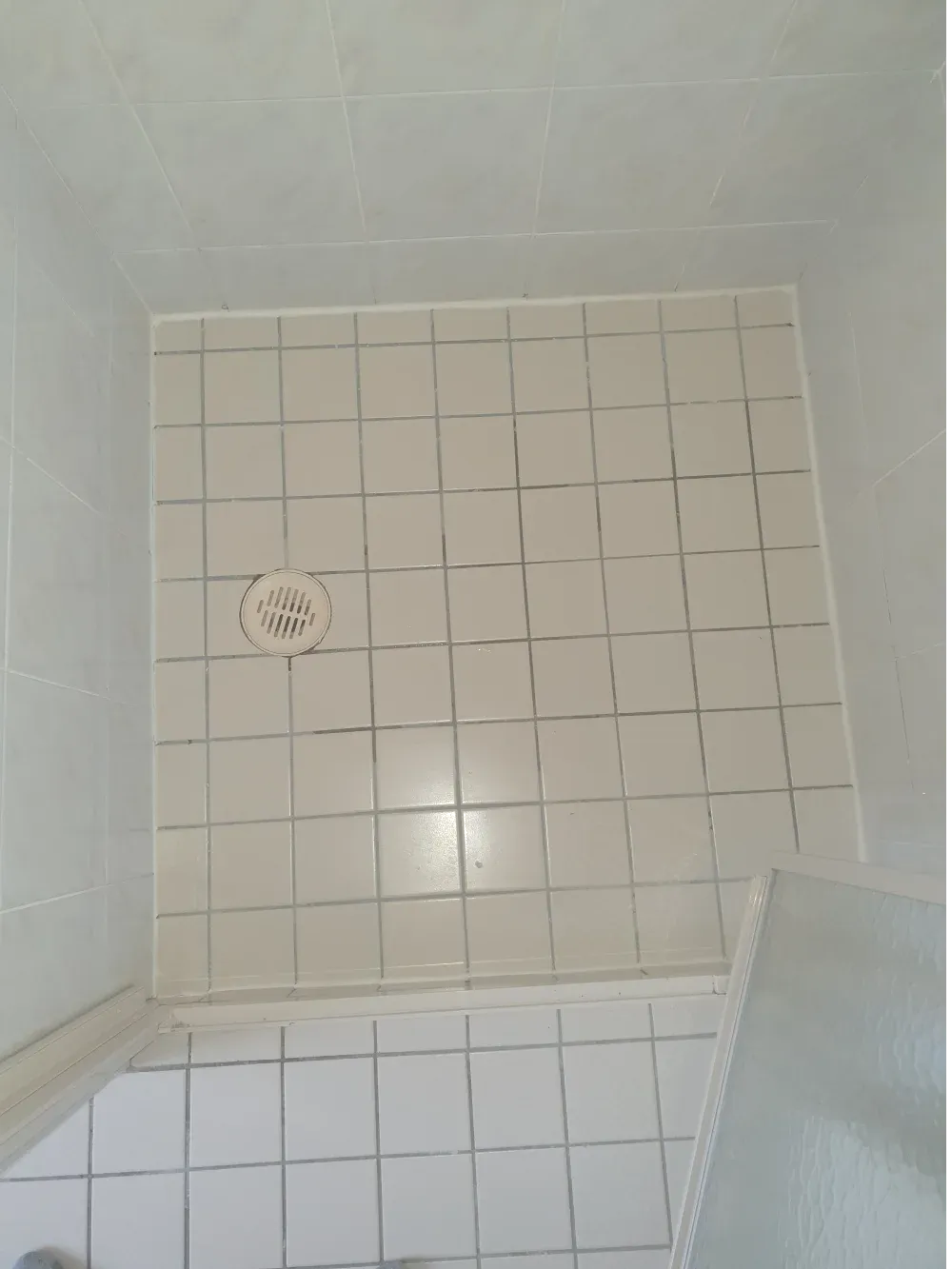 Tiled shower floor with a round drain and a shower seat in the corner.