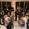 Cena de gala con música en vivo, invitados sentados en mesas redondas y aplaudiendo en un luminoso salón de baile.
