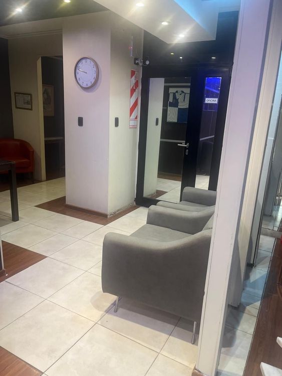 Vestíbulo moderno con asientos grises, reloj de pared, suelo de baldosas y un poste de barbero cerca de una puerta.