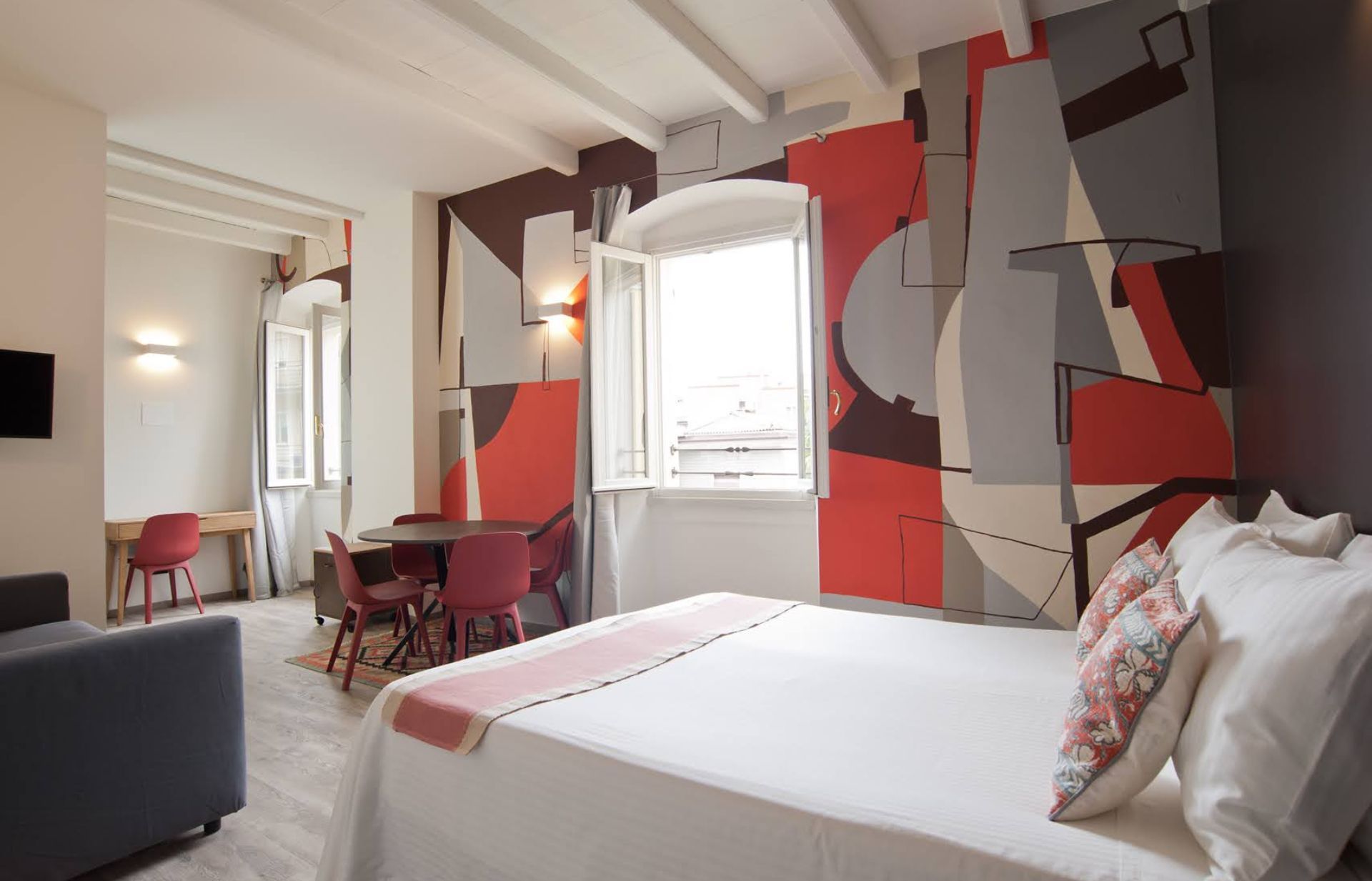 Camera da letto dai colori vivaci con un murale, un letto, un tavolo, sedie e una finestra.