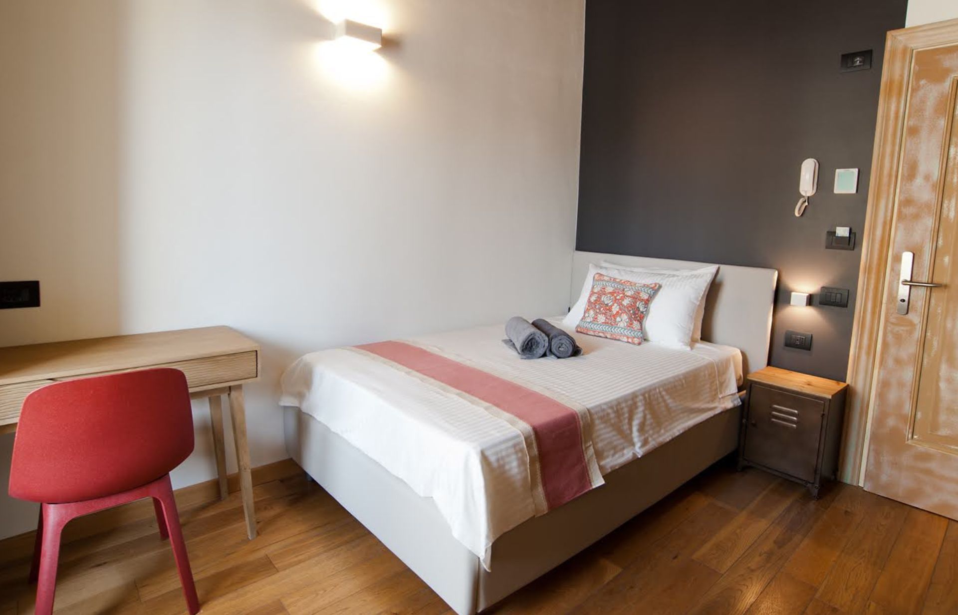Camera da letto con letto singolo, scrivania e porta in legno. Presenta dettagli di colore grigio, bianco e rosso.