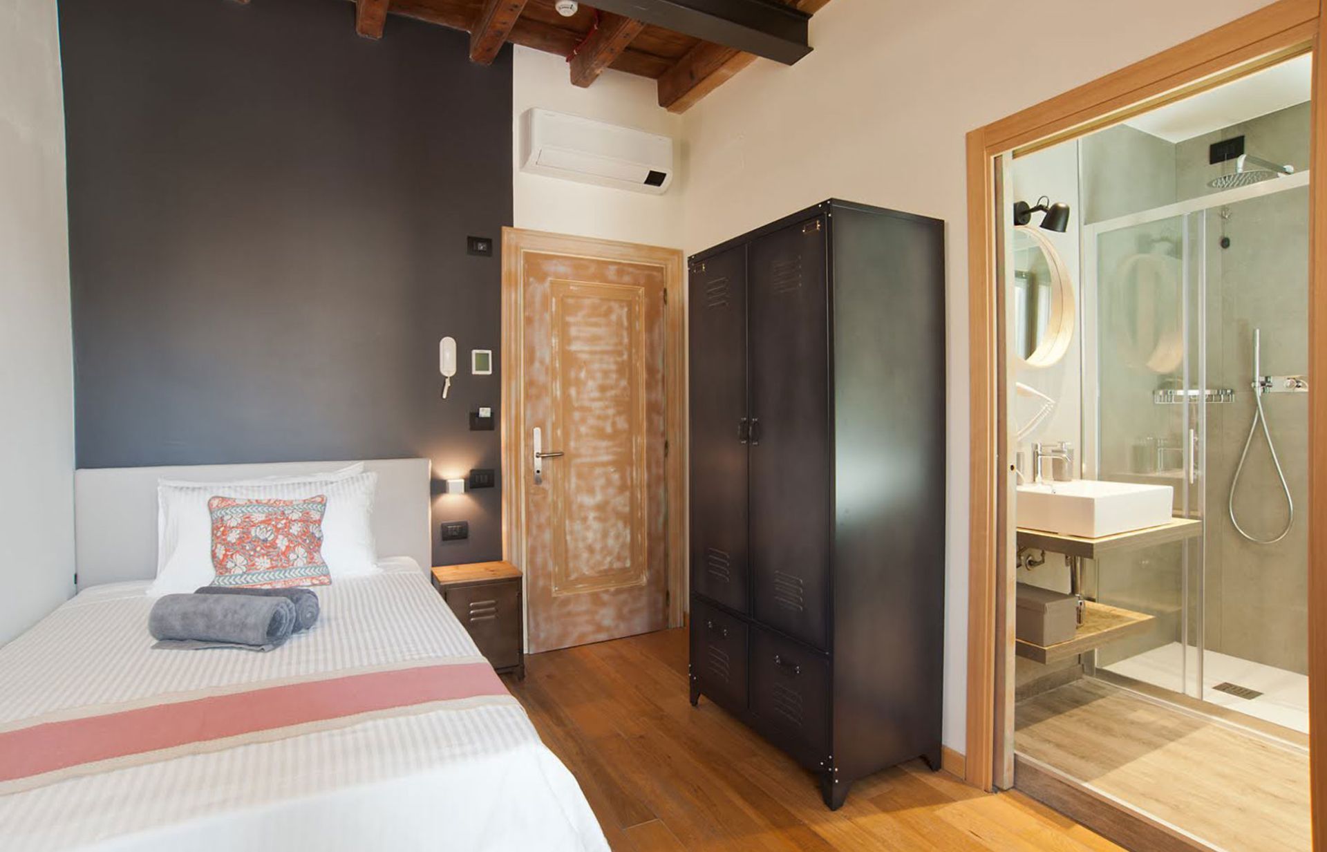 Camera da letto con letto singolo, armadio scuro, porta in legno e bagno con doccia.