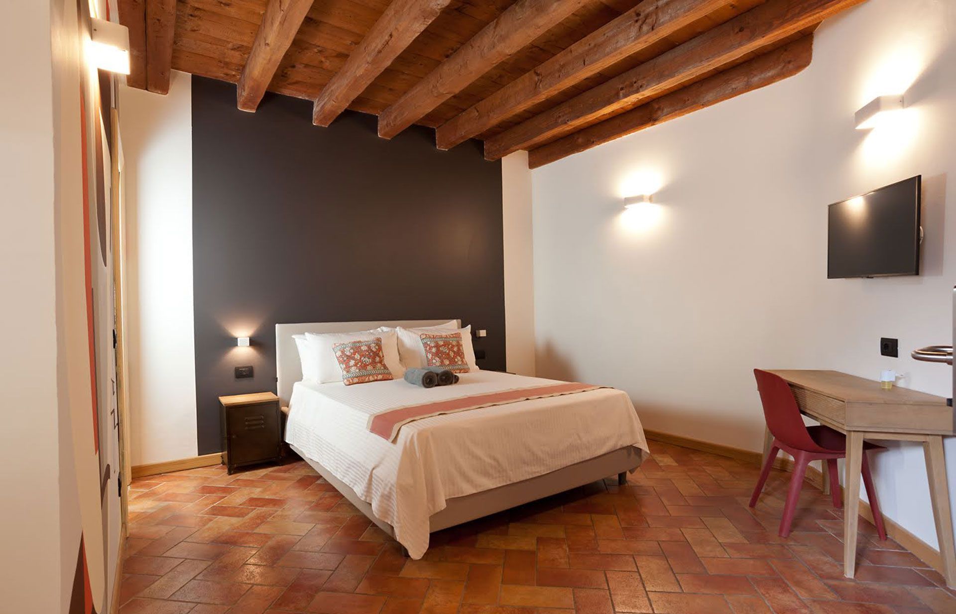 Camera da letto con letto, scrivania e travi in ​​legno a vista. Parete decorativa grigio scuro, pavimento in legno chiaro.