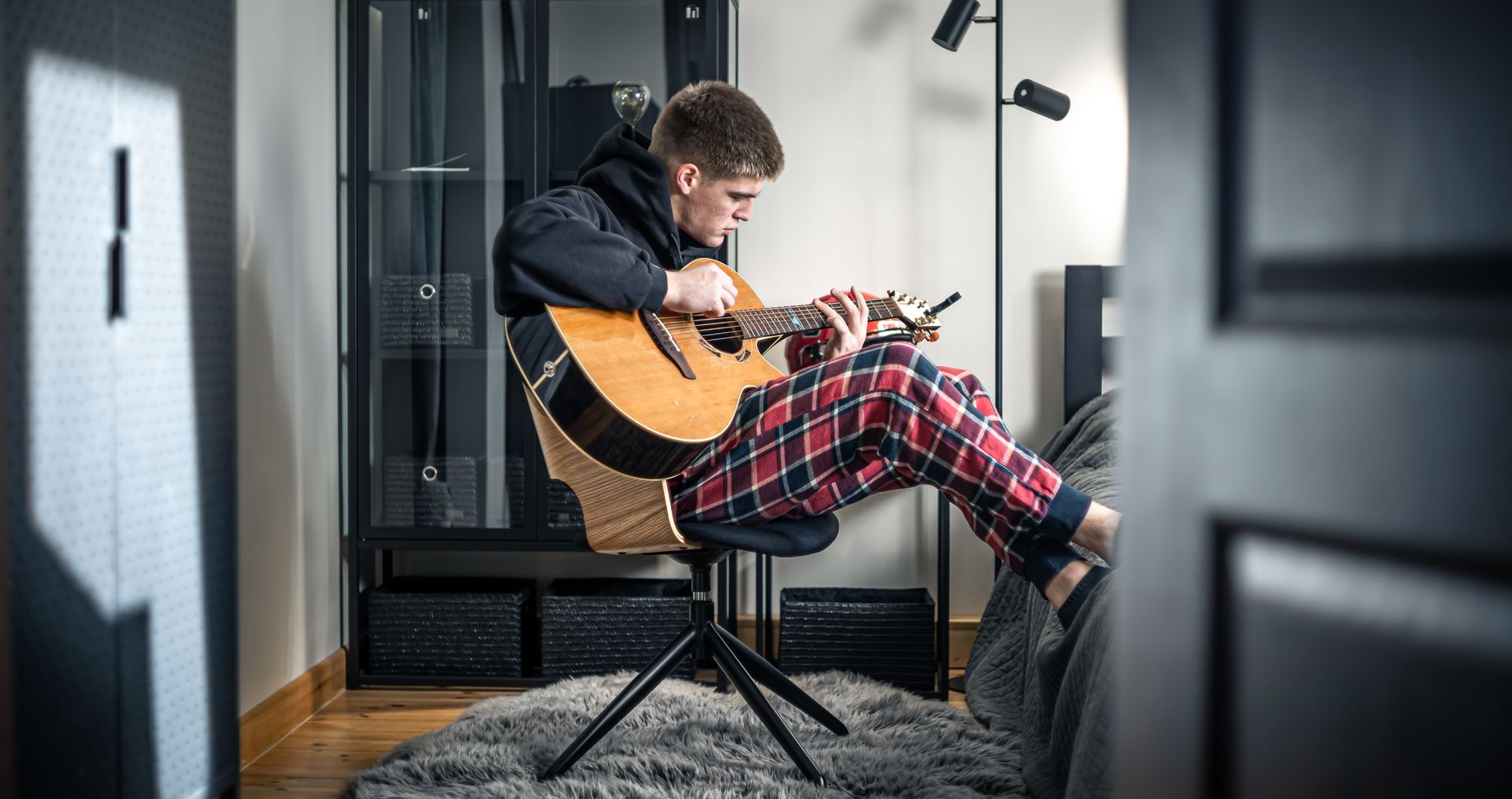 Un uomo in pigiama suona la chitarra acustica, in casa, seduto su uno sgabello.