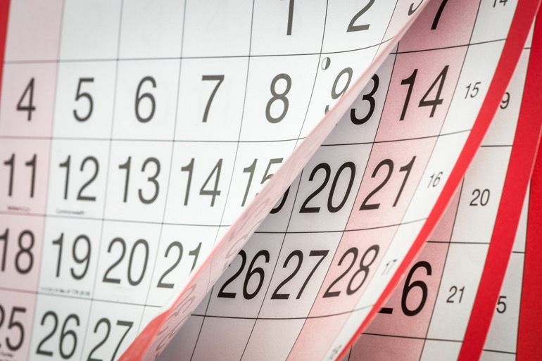 Close-up of a wall calendar with pages turning, showing numbered dates in black, red, and gray.