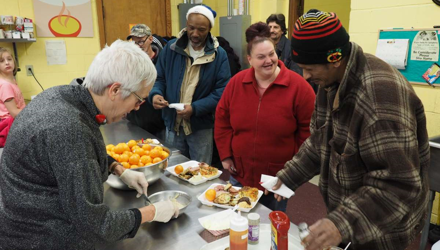 A volunteer serves food in a soup kitchen