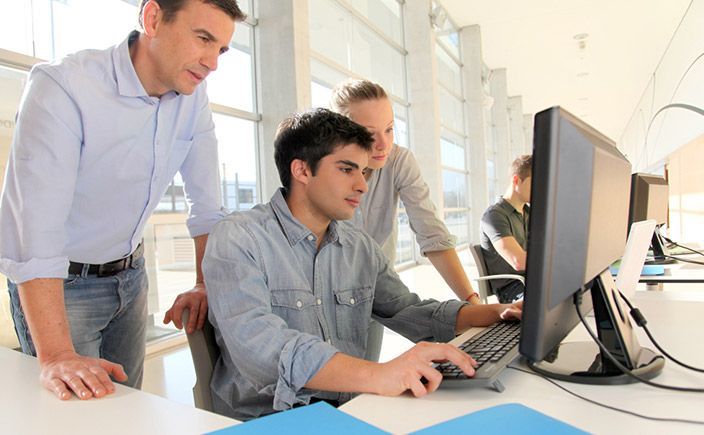 Three members of staff surround a computer to solve an issue