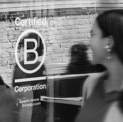 B Corporation certified logo on a storefront window with a blurred passerby in front