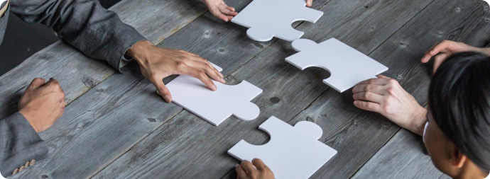 Hands assembling white jigsaw puzzle pieces on a gray wooden table