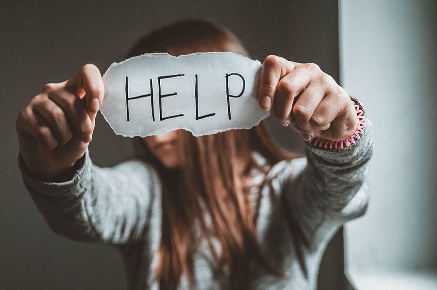Person holding a torn paper sign reading “HELP” toward the camera.
