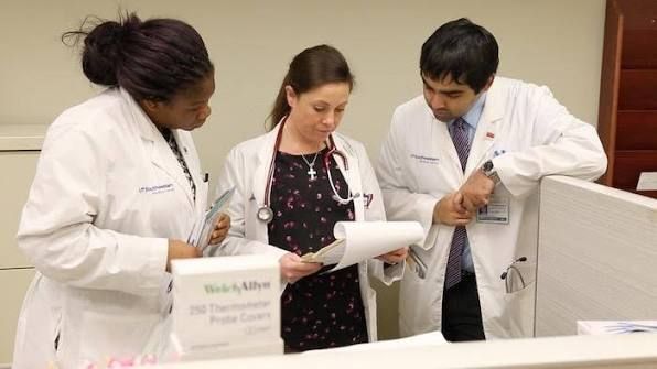 Three medical staff in white coats reviewing a document together in a clinic